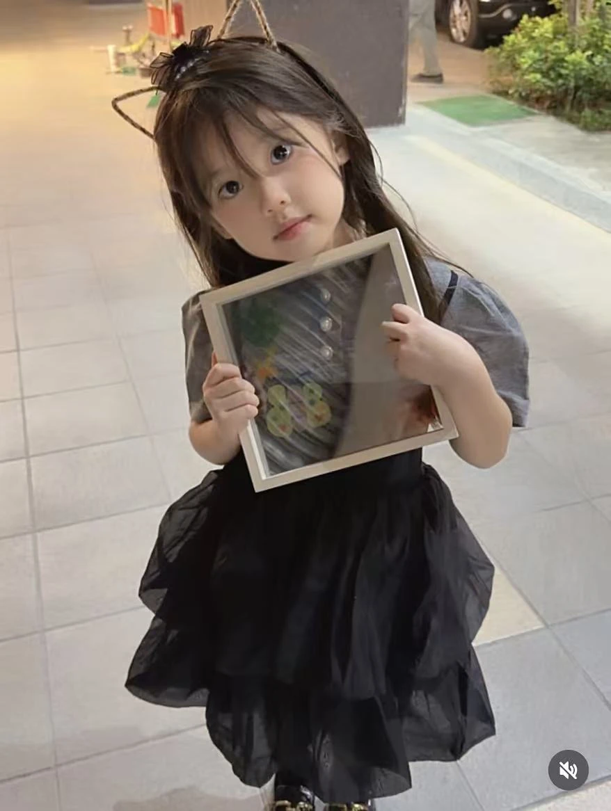 A girl in a cat-ear hair accessory holds a frame in both hands.