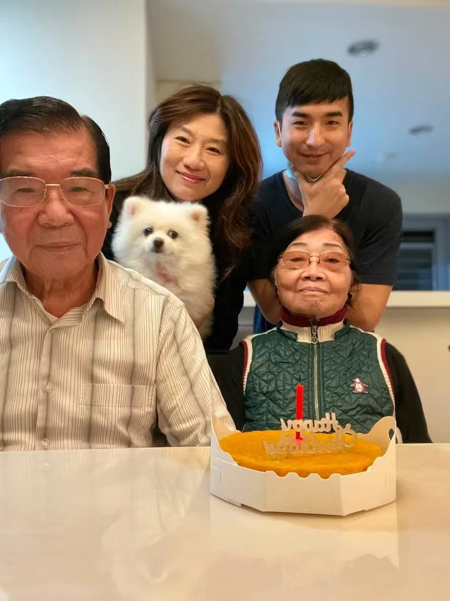 Four family members and a small white dog pose together, with a cake in front.
