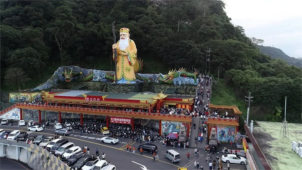 Scene reference photograph of Nanshan Fude Temple at Hongludi: a golden deity statue and two dragons above the temple, with people on the hillside steps to the right.
